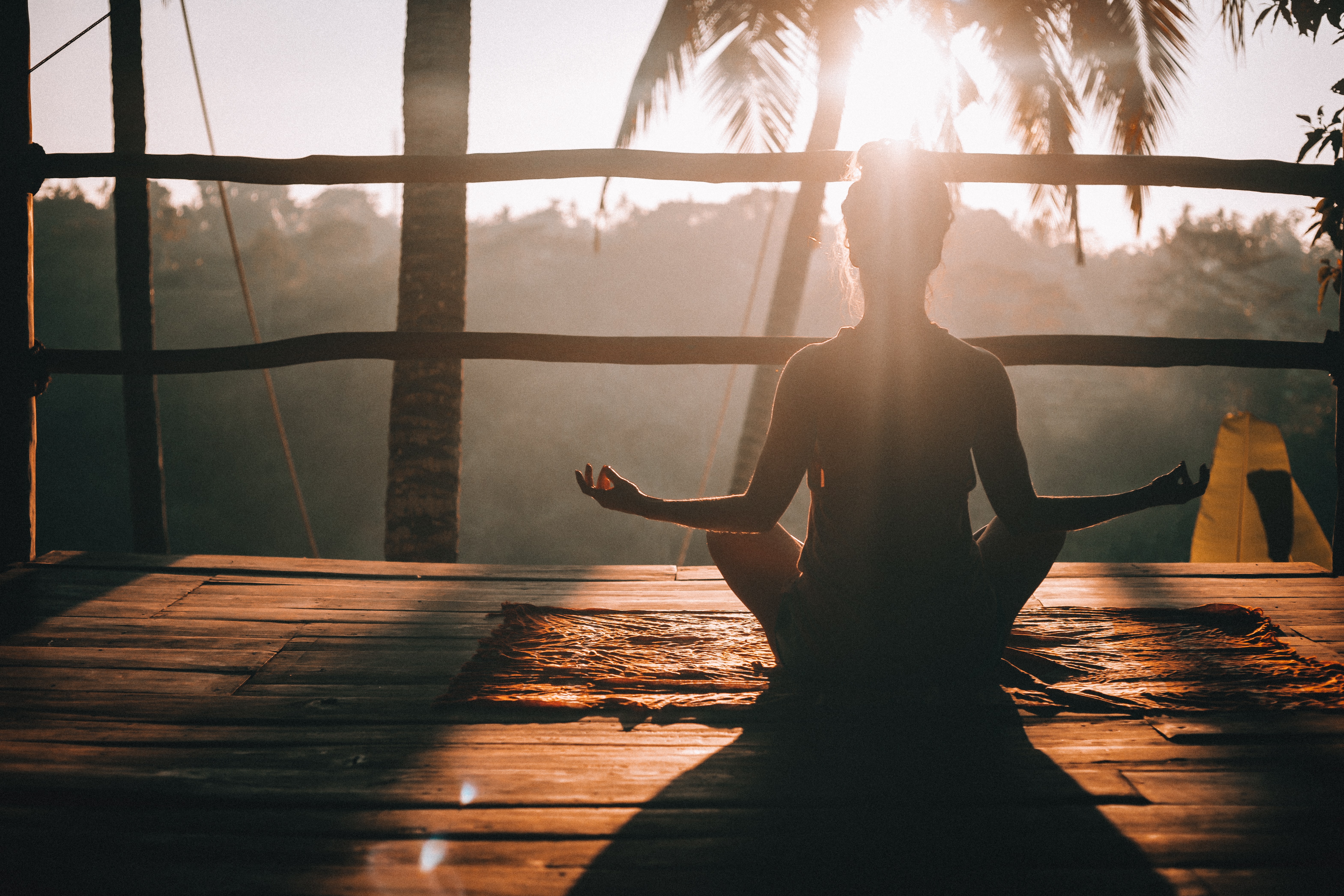 Femme de dos méditant devant un lever de soleil dans une cabane dans la jungle